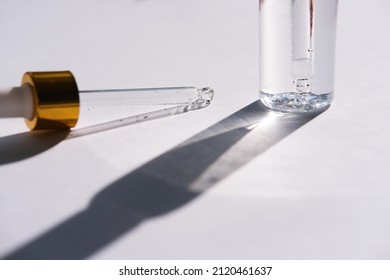 A Glass Pipette And A Cosmetic Bottle Cast A Shadow On A White Background. Side View.