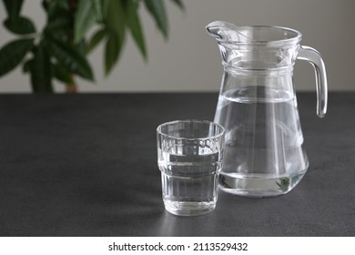 Glass and pitcher of clean water   on a dark table, green plant, copy space background.