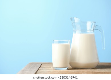 Glass and pitcher of fresh milk on wooden table with light blue background. - Shutterstock ID 2303146941