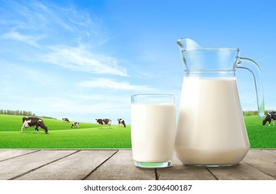 Glass and pitcher of fresh milk on wooden table with grass field and cows background. - Powered by Shutterstock