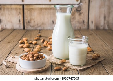 Glass And Pitcher With Vegan Almond Milk, Almond Kernels And Whole Almonds On An Old Rustic Wooden Table