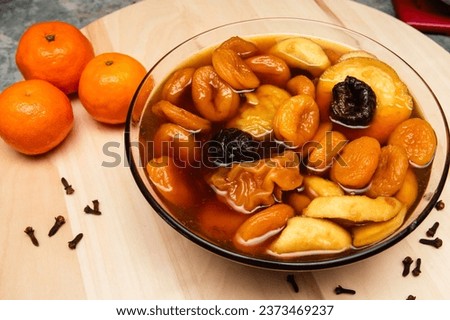 Glass platter with a Christmas compote made of dried fruit, next to cloves and mandarins (selective focus)