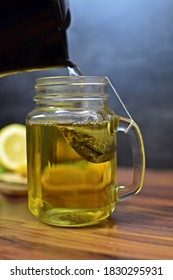 A Glass Is Poured With Hot Water And A Tea Bag For Peppermint Tea Hangs Inside. Fresh Peppermint Tea Is Boiled Up, Suitable For The Winter And Flu Season