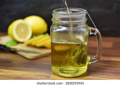 A Glass Is Poured With Hot Water And A Tea Bag For Peppermint Tea Hangs Inside. Fresh Peppermint Tea Is Boiled Up, Suitable For The Winter And Flu Season