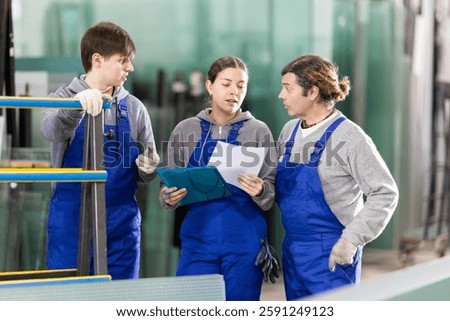 In glass processing workshop, girl supervisor with documents and two male workers, conducts survey of contractor, writes down information about work performed.