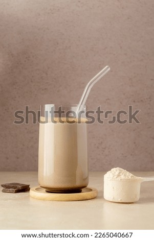 Glass of protein shake drink with protein powder scoop and glass straw.