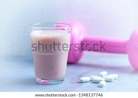 Glass of Protein Shake with milk and raspberries. BCAA amino acids and pink dumbbell in background. Sport nutrition. Stone / Wooden background. Copy space. 
