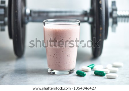 Glass of Protein Shake with milk and raspberries. BCAA amino acids, L - Carnitine capsules and a dumbbell in background. Sport nutrition. Stone / Wooden background. Copy space. 