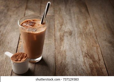 Glass With Protein Shake And Powder In Scoop On Wooden Table