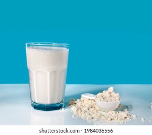 Glass Of Protein Shake And Spoon Of Protein Powder On A Blue Background.