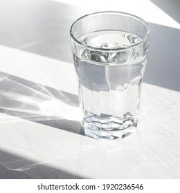 A Glass With Pure Clear Melt Water Stands On A White Wood Table