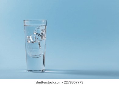 Glass of pure cold sparkling water with ice cubes on light blue background. Free space for text