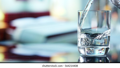 A Glass Of Pure Fresh Water Is Poured Into A Glass, The Background Bedroom, Nature, From Which The Fresh And Pure Water. Concept: Nature, Purification, Freshness.