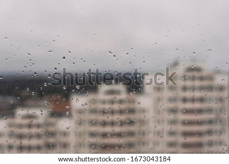 Glass with raindrops on the background of multi-storey buildings shot with shallow depth of field.