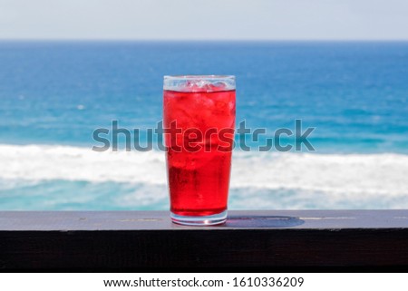 a glass of red colddrink on a wooden table with the ocean in the background