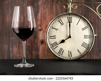 Glass Of Red Wine With Antique Clock On Wooden Background, Concept Image For Dinner Time Or Alcoholism In The Evening After Work