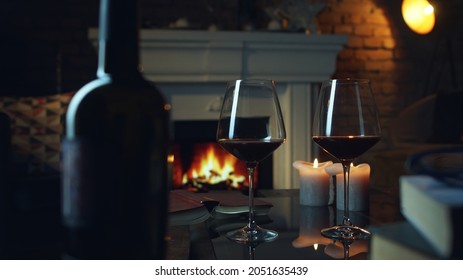 Glass Of Red Wine, Book And Candle On Table In Dark Room With Fireplace. Cozy Warm Home In Winter.