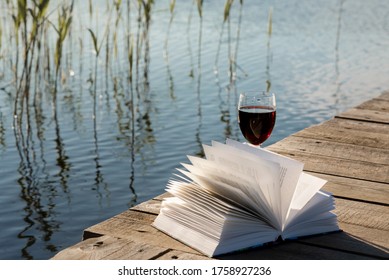 Glass Of Red Wine And A Book On The Pier On The Lake. 