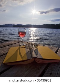 Glass Of Red Wine, Book, And Sunglasses On A Dock At A Lake