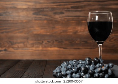 A glass of red wine and a bunch of dark grapes are arranged on a rustic wooden surface with a wood grain background. Ideal for wine tasting, vineyard, or culinary themes  - Powered by Shutterstock