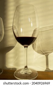 Glass With Red Wine With Dark Reflection Into Sin Light On Table 