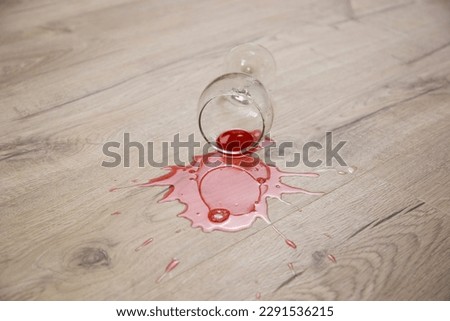 Glass of red wine fell on laminate, wine spilled on floor.