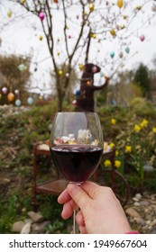 Glass Of Red Wine In The Female Hand And Easter Tree With Decoration And Festive Breakfast Brunch On The Retro Mobile Table  In The Garden. Nature Background.