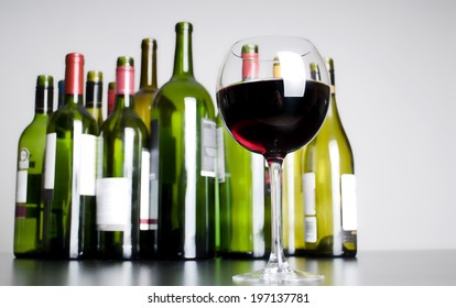 Glass of red wine in front of many empty wine bottles.