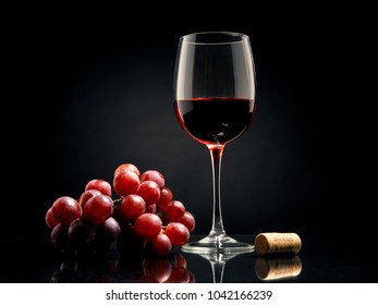 Glass of red wine with grapes and cork on black background