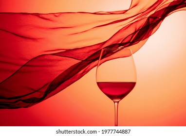 Glass Of Red Wine On A Background Of Waving Black Satin Curtain. Red Backlit.