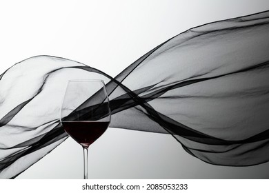 Glass Of Red Wine On A Background Of Waving Black Satin Curtain.