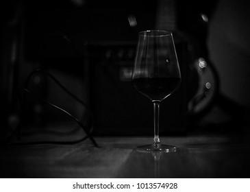 Glass Of Red Wine On A Floor Near Bass Guitar. Lonely Saturday Nights Of A Musiacian At Home.