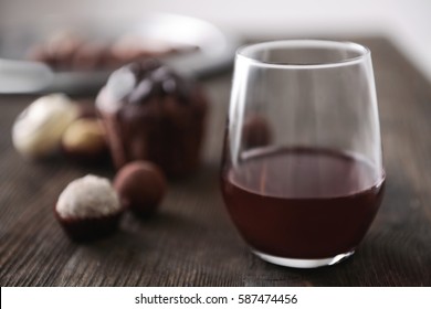 Glass with red wine on wooden table and blurred background of delicious chocolate candies