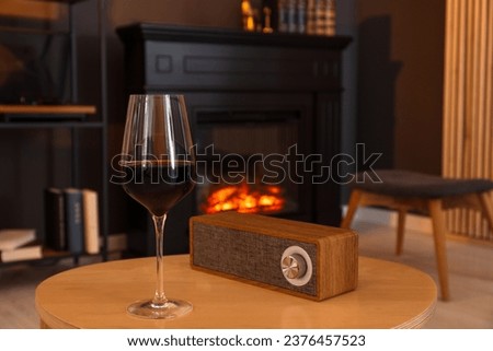 Glass of red wine and portable speaker on table in room. Relax at home