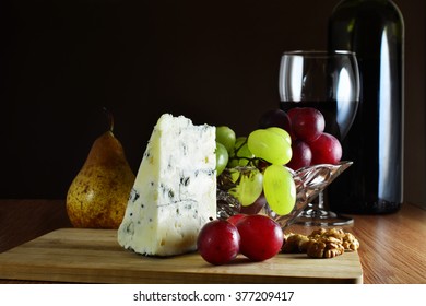 Glass of red wine with a wedge of French blue cheese, grapes and fruits on wooden board.