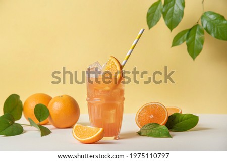 A glass of refreshing orange juice with a slice of orange and ice on a yellow background with juicy fresh fruit oranges. Top view and copy space image