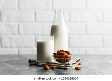 Glass reusable bottle and mug with almond milk and almonds on a marble countertop, kitchen with a white brick wall.