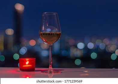 A Glass Of Rose Wine With Red Candle On Table And Colorful City Bokeh Light Background.