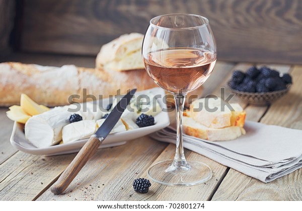A glass of rose wine served with cheese
plate, blackberries and baguette. Assortment of cheese with berries
on wooden background.
