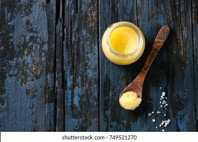 Glass of salted drawn ghee butter standing with wood spoon and sea salt over old dark blue wooden background. Healthy eating. Top view, copy space