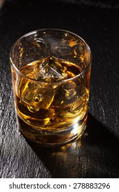 Glass Of Scotch Whiskey With Ice On Black Stone Table