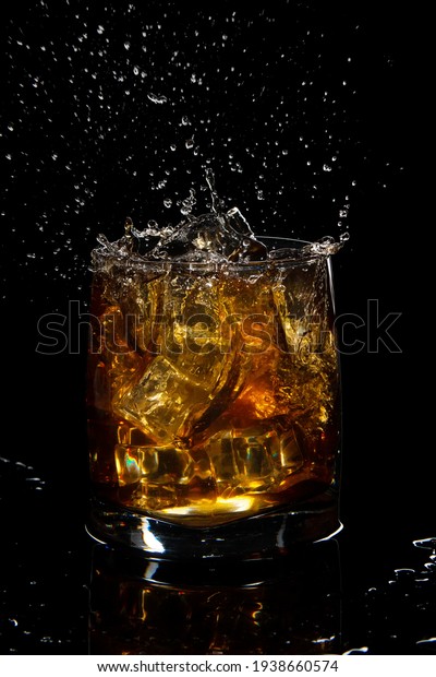 glass of scotch whiskey with splash and ice on\
black background
