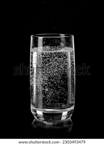 Glass of soda water with bubbles on black background
