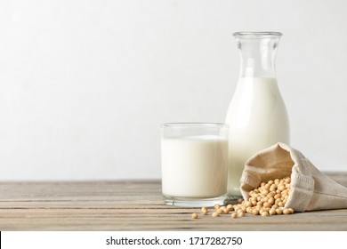 Glass of soy milk with bottle and soybeans on wooden table.