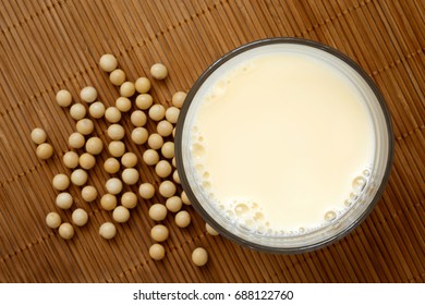 Glass Of Soya Milk With Froth On Bamboo Mat From Above. Spilled Soya Beans.