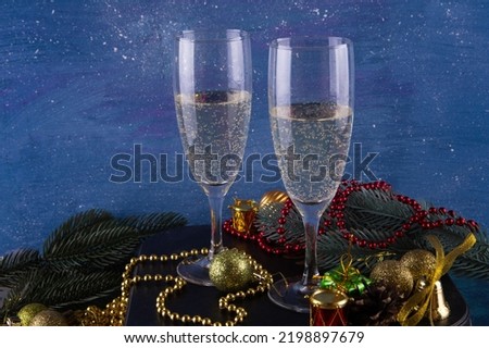 Glass with sparkling shampagne on blue Christmas background. Different holiday decorations around