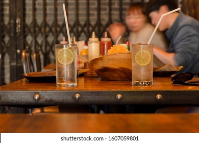 Glass Of Sparkling Water And Slice Of Lime With Blurred People In Blackground