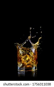 Glass Of Splashing Whiskey Or Other Alcohol With Ice Cube Isolated On Black Background