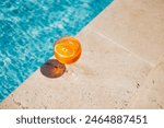 Glass of spritz aperol with orange slice against poolside at resort hotel during vacation. Elegant goblet of sparkling wine and orange juice on background of blue water outdoor. Relaxation and travel.