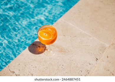 Glass of spritz aperol with orange slice against poolside at resort hotel during vacation. Elegant goblet of sparkling wine and orange juice on background of blue water outdoor. Relaxation and travel. - Powered by Shutterstock